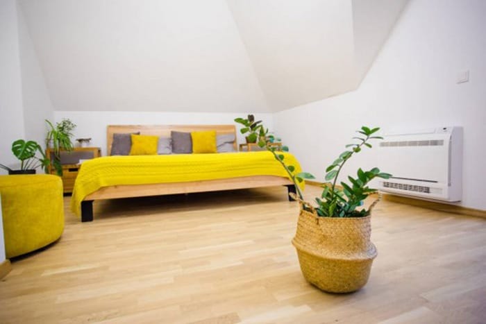 Habitación con suelo de madera, cama de matrimonio con sabanas amarillas y plantas