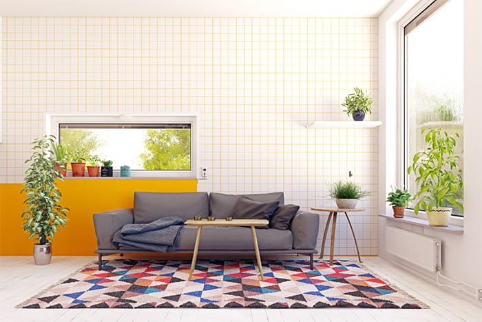 Pequeño espacio de descanso con alfombra estampada con motivos geométricos y pared decorada a cuadros mediante pintura sectorizada