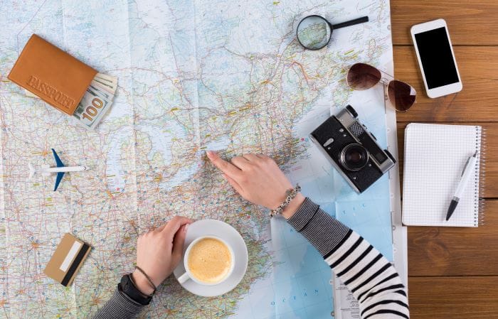 Persona organizando un viaje con un café, un mapa y algunos objetos de viaje