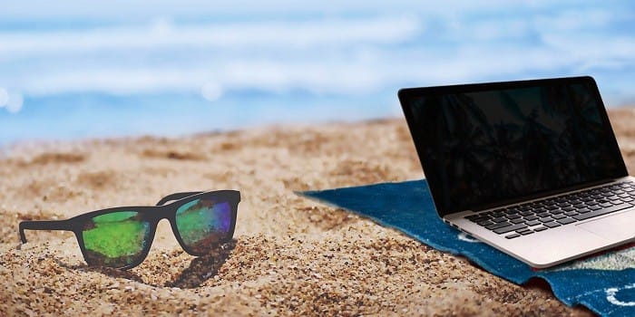 gafas de sol y portátil en la arena de la playa
