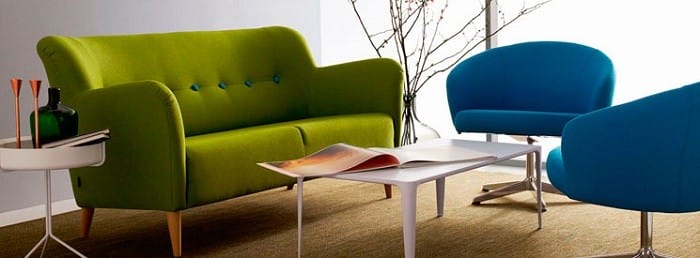 salón con sofá verde y dos sillas azules con mesa auxiliar pequeña