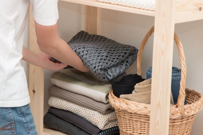 un chico dejando ropa doblada en una estantería de madera