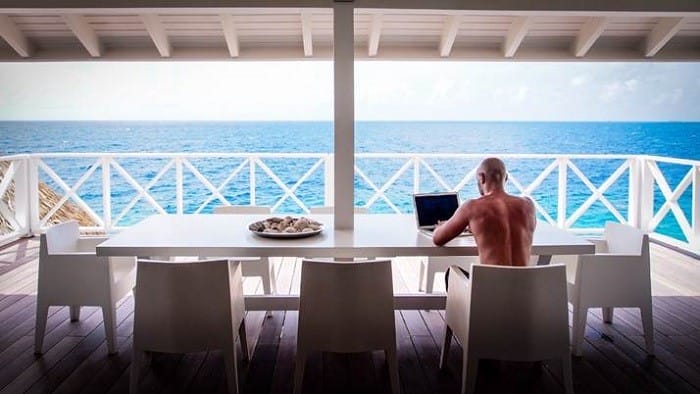 Chico teletrabajando con el ordenador en la playa