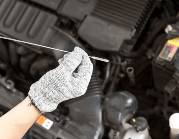 Persona con guantes midiendo el aceite del coche