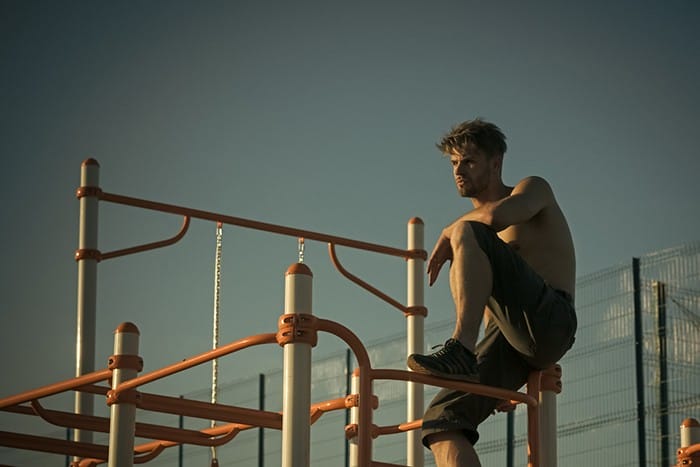 Climb, climbing frame. Man sit on metal jungle gym on blue sky. Sport, health, recreation. Sportsman with bare torso on monkey bars top. Freedom, success, energy concept.