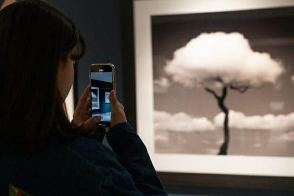 Chica haciendo una foto con el móvil a un cuadro de fotografía de la exposición de Chema Madoz en Granada "En torno al tiempo"