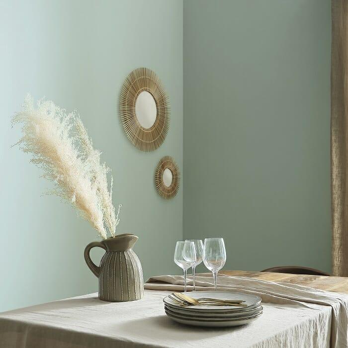 Salón con mesa puesta y pared verde con espejo moderno