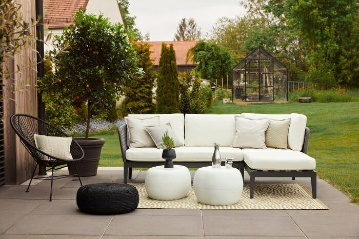 Zona de exterior con sofá blanco, silla, puffs y mesitas westwing