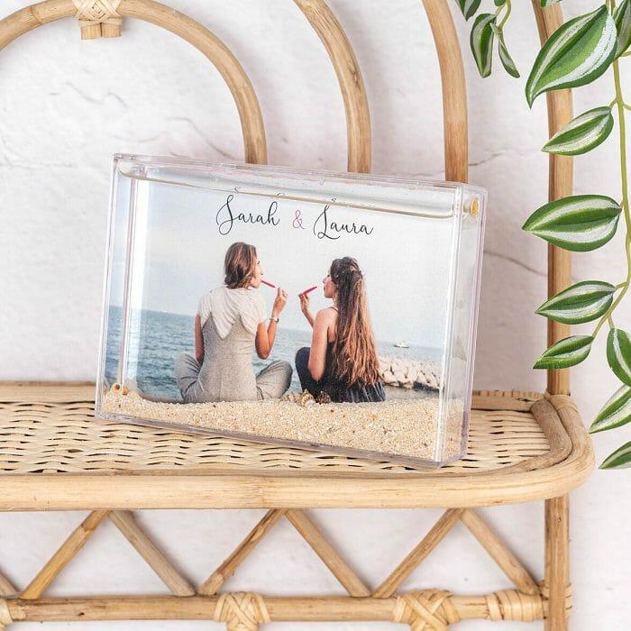 Bola de nieve rectangular con una fotografía dentro de una pareja en la playa. Objeto decorativo en una estantería