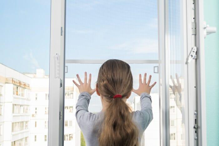 Niña cerca de una ventana tocando la mosquitera enrollable