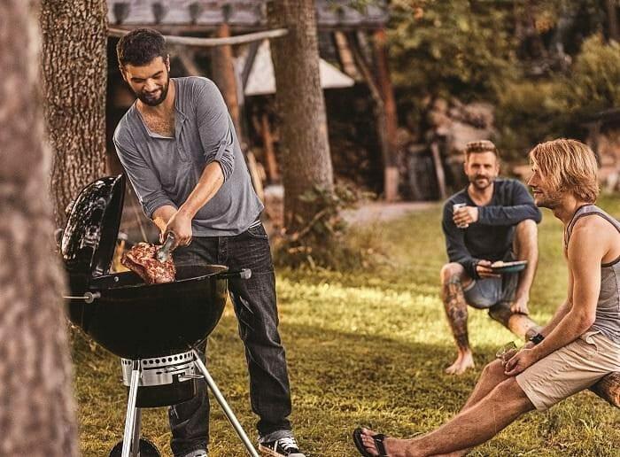 Grupo de amigos en el exterior disfrutando de una barbacoa de carbón con tapa
