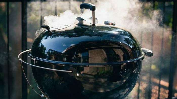 Barbacoa redonda de carbón echando humo con tapa