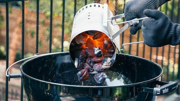 Persona echando carbón a una barbacoa de carbón encendida