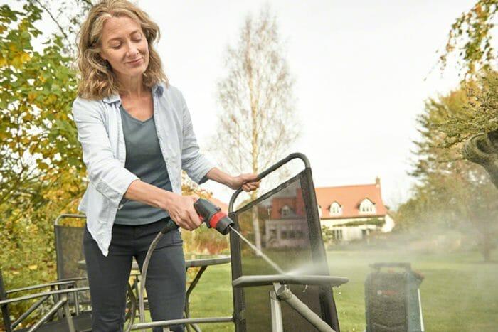 Mujer con máquina para limpiar de Bosch limpiando una silla de jardín