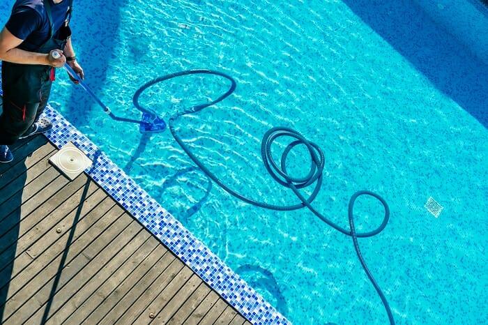 Persona pasando un limpiafondos manual por una piscina