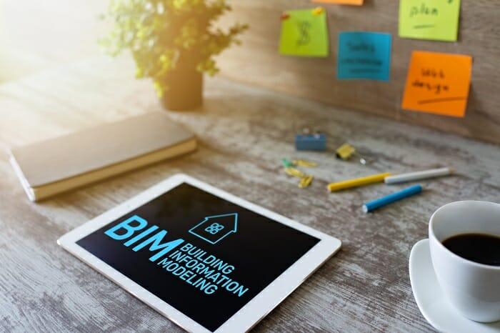 Pantalla de tablet con letras BIM encima de un escritorio con café y bolígrafos