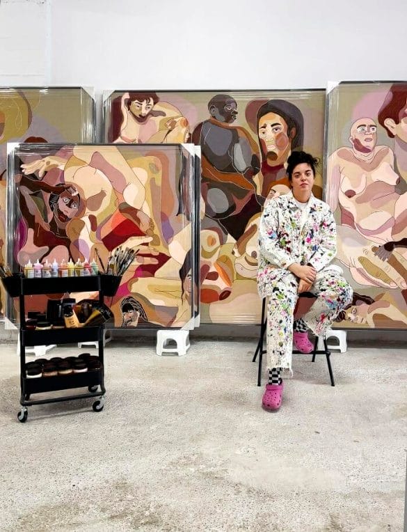 La artista pintora Ela Fidalgo sentada al lado de sus cuadros