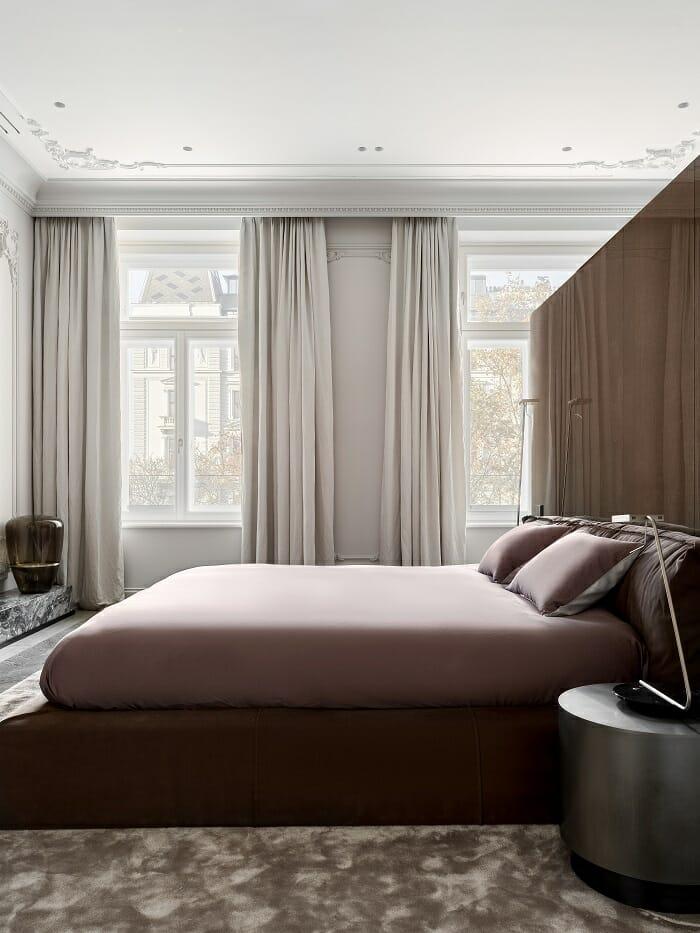 Habitación con cama y de fondo grandes ventanales con cortinas