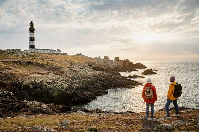 Pareja de turistas en la isla de Ouessant con un faro al fondo