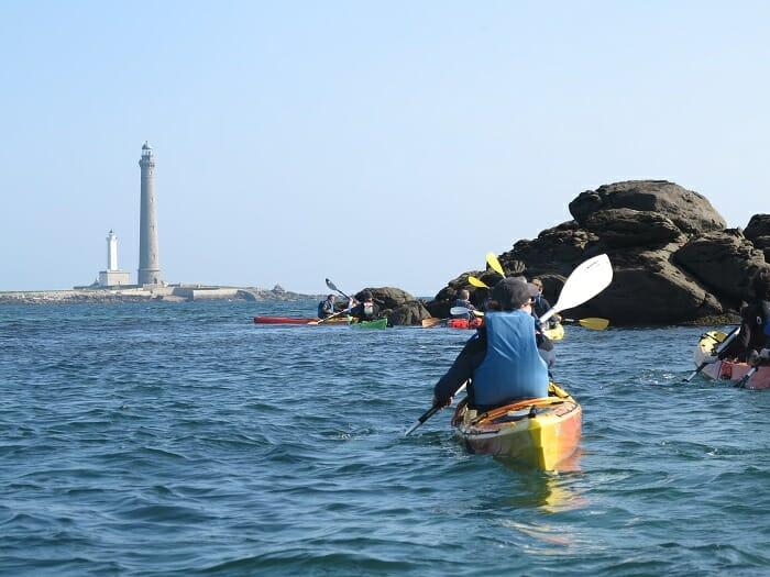 Pareja haciendo kayak en el mar con un faro bretón al fondo