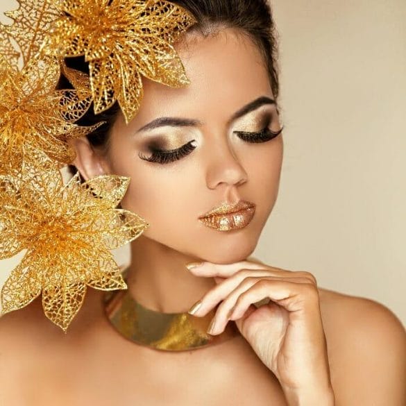 Rostro de una mujer joven con maquillaje en tonos dorados y tierra con colgante y adorno en el pelo dorados
