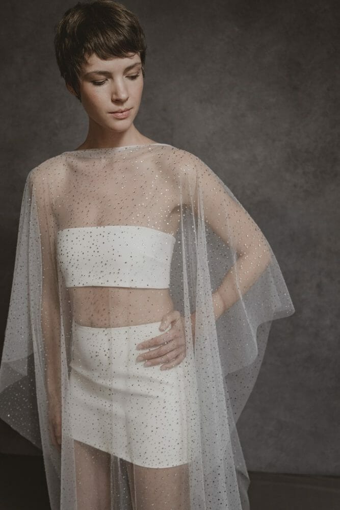 Modelo llevando un top y falda blancos con un poncho encima transparente