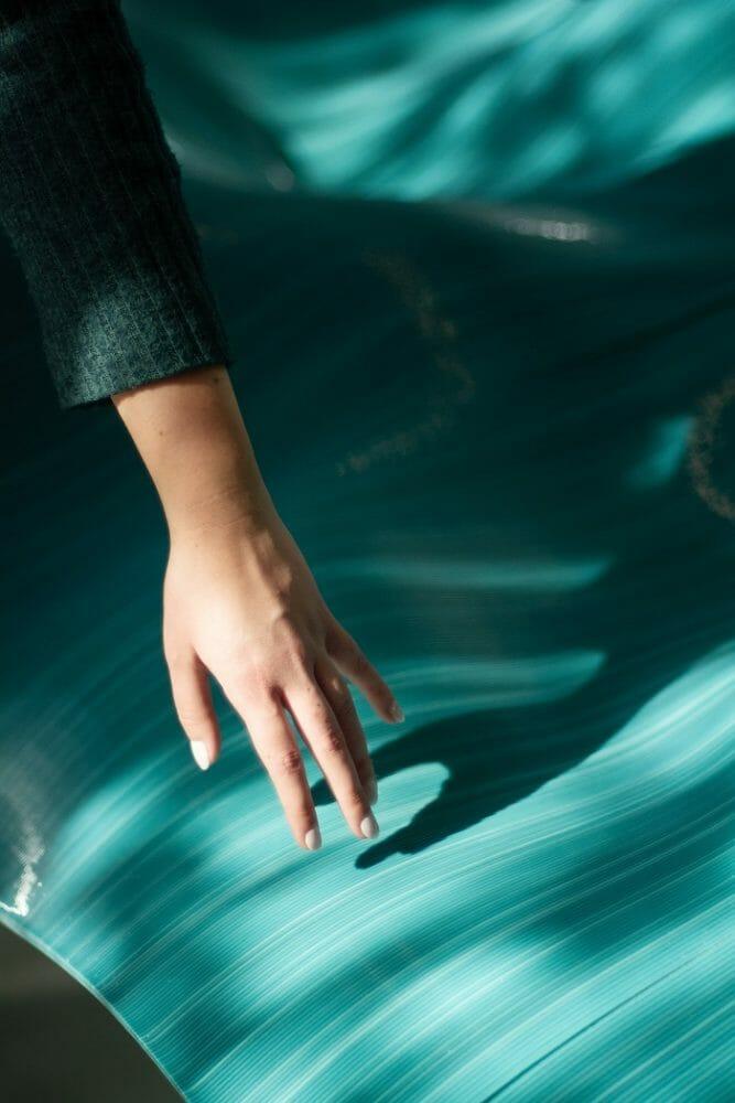 Mano tocando la tela que simula el mar de la exposición Beyond the plastic wave en Barcelona