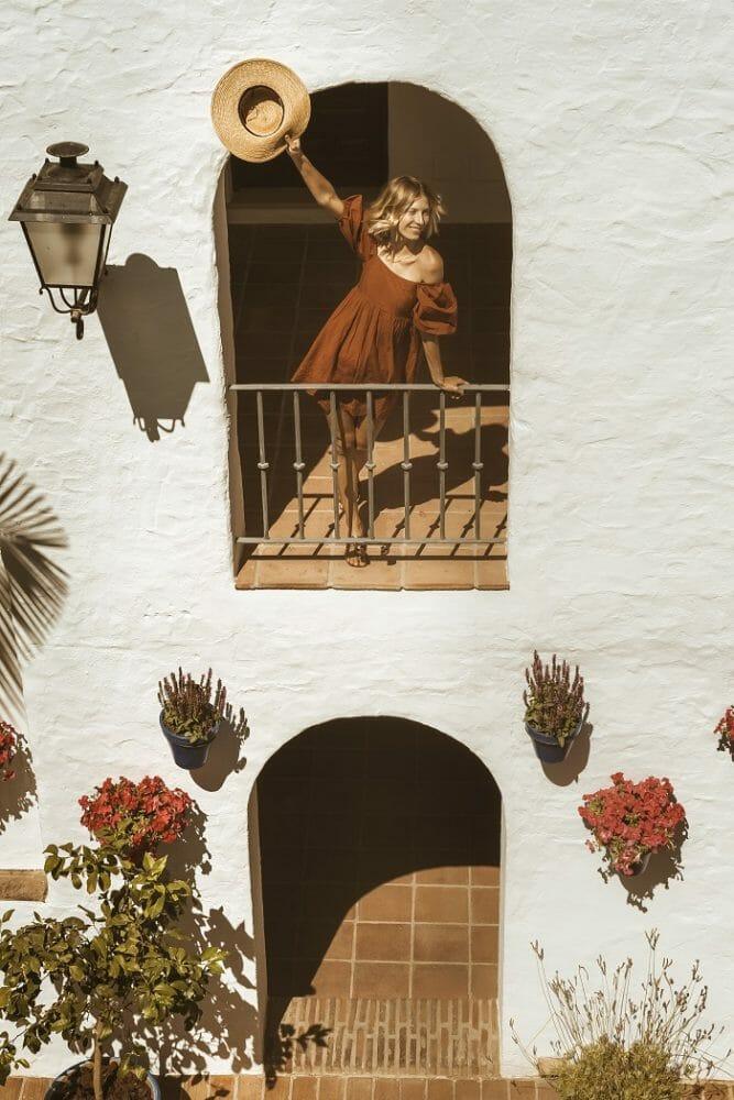 Fachada con flores y una mujer asomada en un balcón de Puente Romano