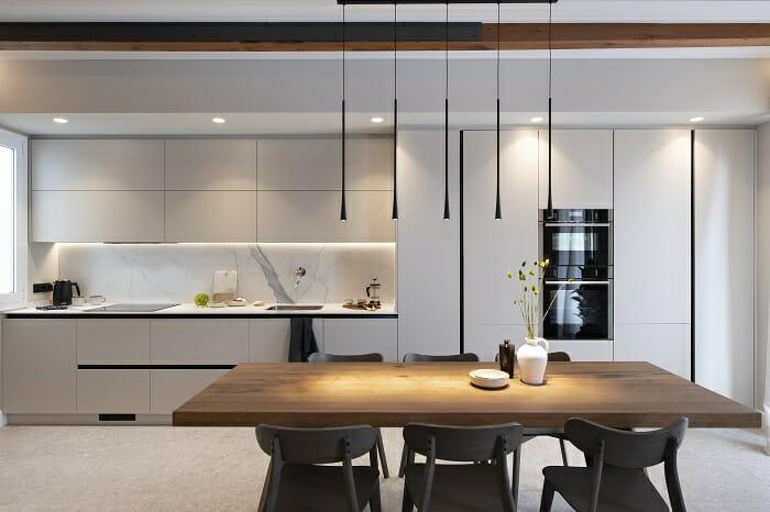 Diseño de una cocina blanca abierta con una mesa de madera con lámparas colgantes