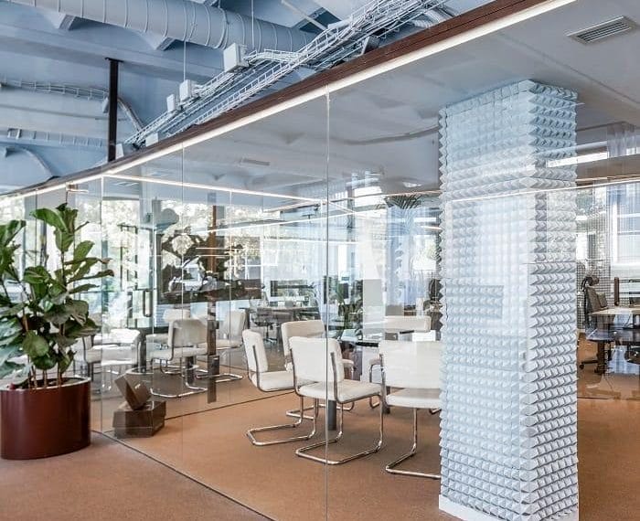 Despacho de Nude Project con planta, sillas blancas y cristalera transparente