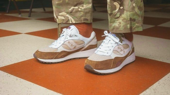 Pies de persona con unas zapatillas de la marca Saucony Original modelo Shadow 6000 en color tierra y beige