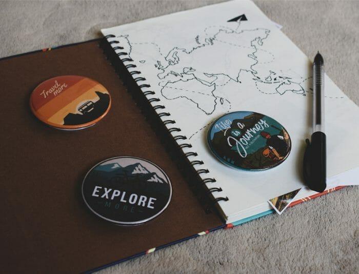 Cuaderno abierto con bolígrafo y encima tres chapas personalizadas