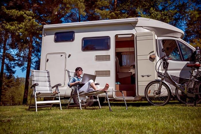 Mujer sentada al lado de su camper leyendo un libro en el campo