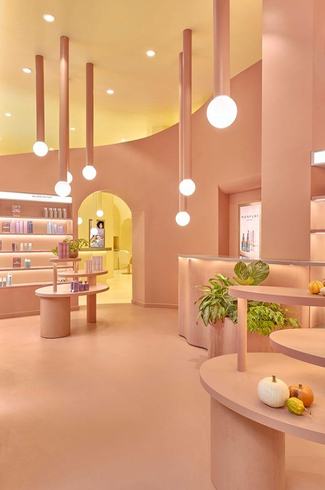 Interior del salón de belleza Emma con lámparas colgantes, mostrador, mesa y estantería color rosas