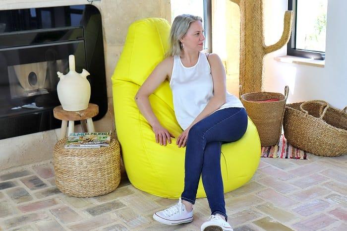 Mujer sentada en un puff amarillo junto a una chimenea