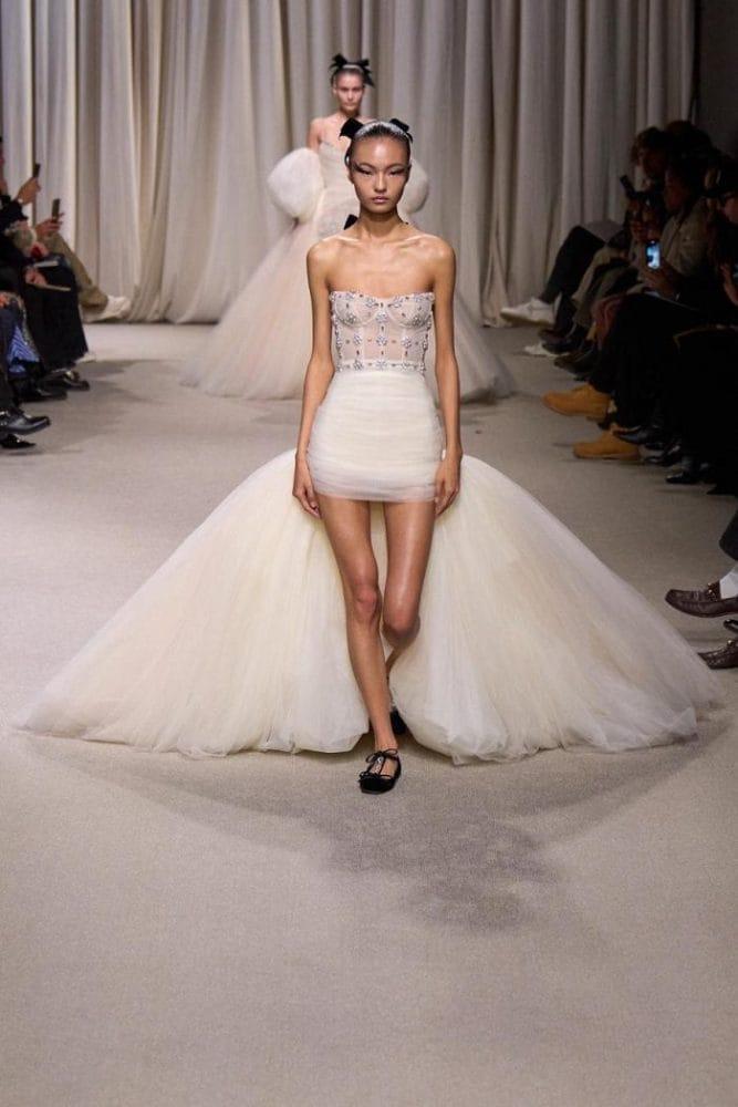 Modelo en pasarela llevando un vestido corto blanco con unas bailarinas negras
