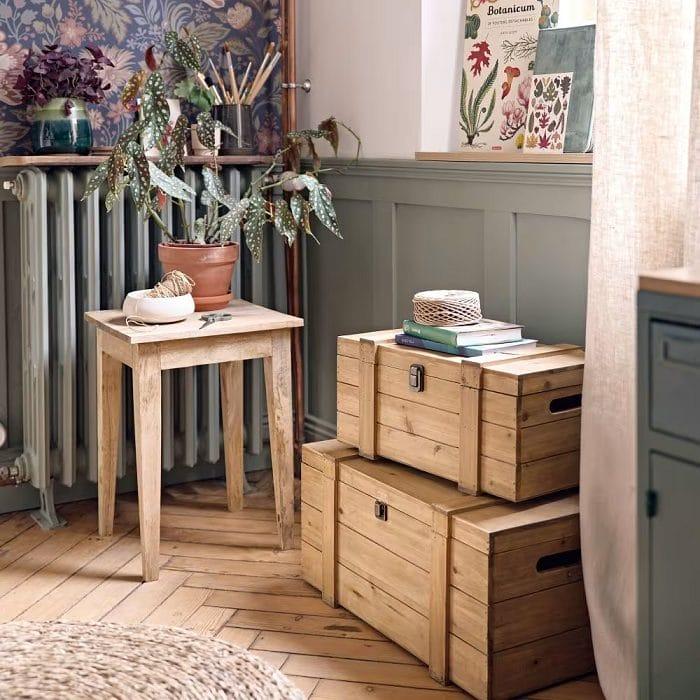 Rincón de un hogar con un taburete de madera con una maceta y dos baúles de madera