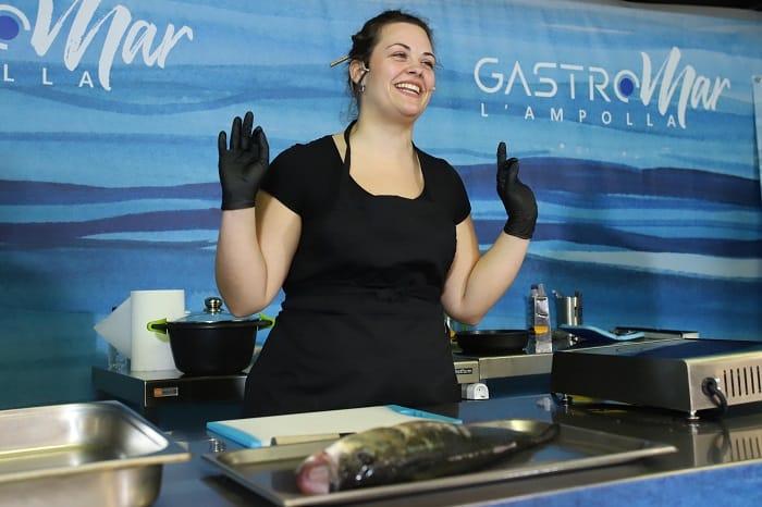 Chica con guantes negros con un pescado crudo en la mesa para cortar