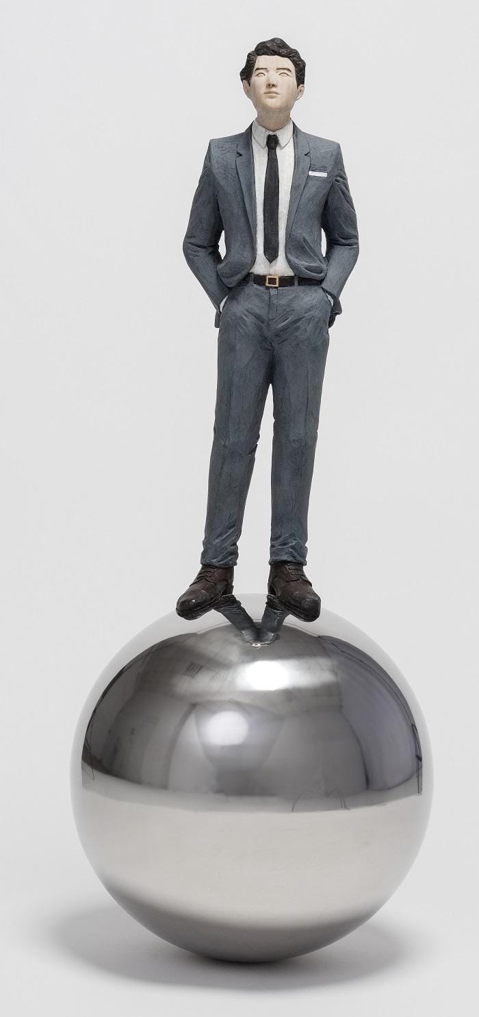 Figura de un hombre en traje subido a una bola plateada