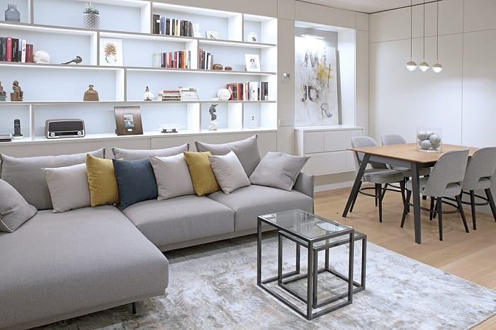 Salón con sofá con cojines y detrás una estantería con iluminación led