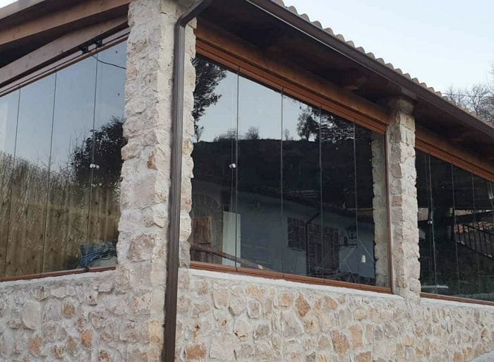 Cortinas y cerramientos de cristal en una fachada de piedra de una casa