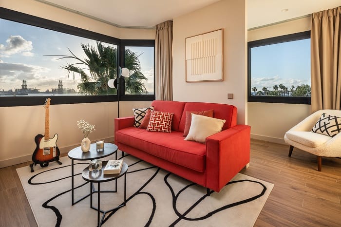 Zona de un salón o sala de espera con sofá rojo con cojines y dos mesas pequeñas