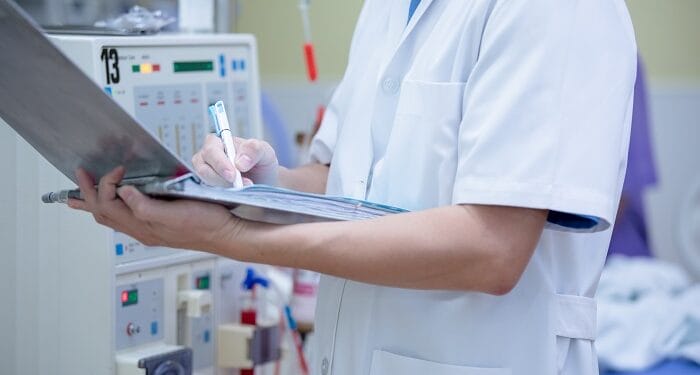 Cuerpo de persona sanitaria con bata blanca escribiendo en su cuaderno en un hospital