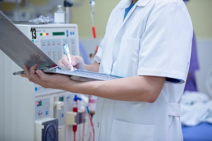 Cuerpo de persona sanitaria con bata blanca escribiendo en su cuaderno en un hospital
