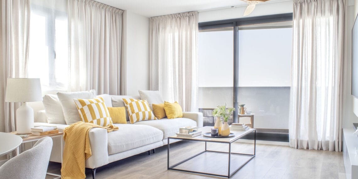 Salón moderno en un piso valenciano con sofá blanco y cojines amarillos, diseñado por Anabel Soria, creando un ambiente fresco y luminoso