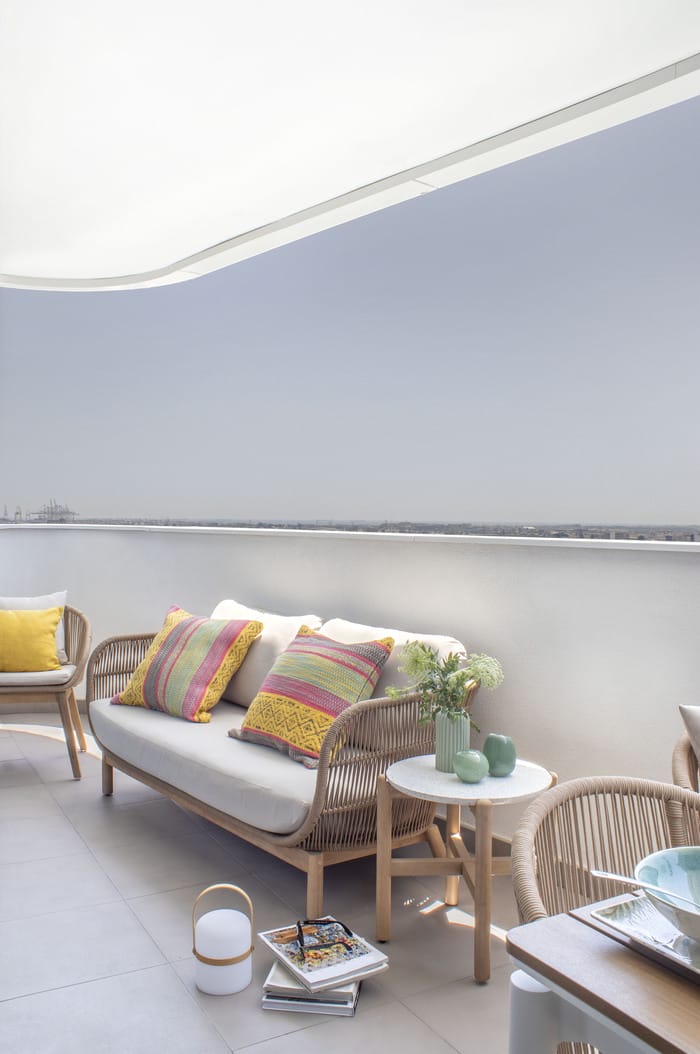 Terraza acogedora decorada con muebles de ratán y cojines coloridos, creación de Anabel Soria en un piso valenciano