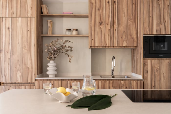 Cocina reformada con península multifuncional, muebles laminados en madera y encimera Dekton Nacre en un apartamento vacacional en Benidorm.