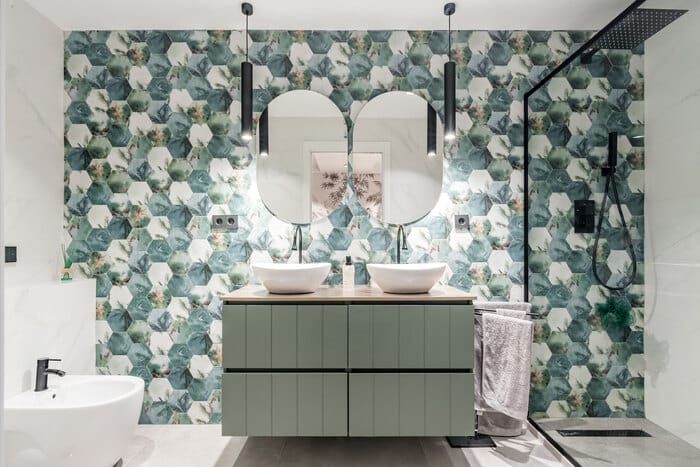 baño con dos espejos ovalados con armario verde y pared con tapiz diseño