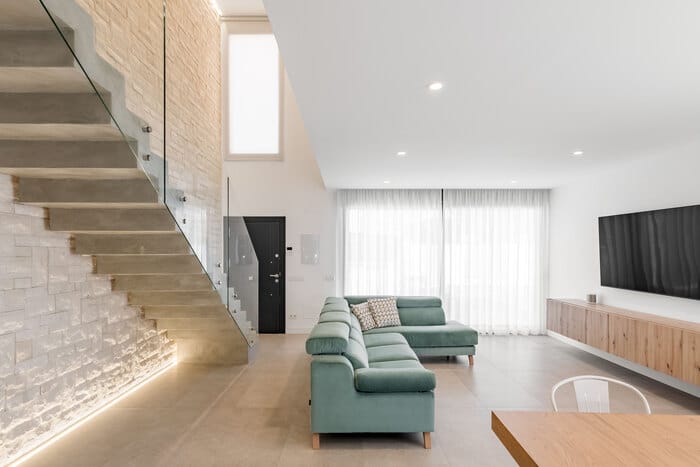 Salón amplio y luminoso con decoración moderna y sofá central en vivienda adosada diseñada por ALEM Arquitectura