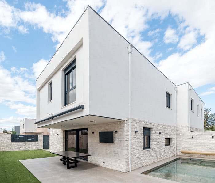 Diseño de fachada de vivienda adosada en piedra blanca con ventanas panorámicas proyecto de ALEM Arquitectura